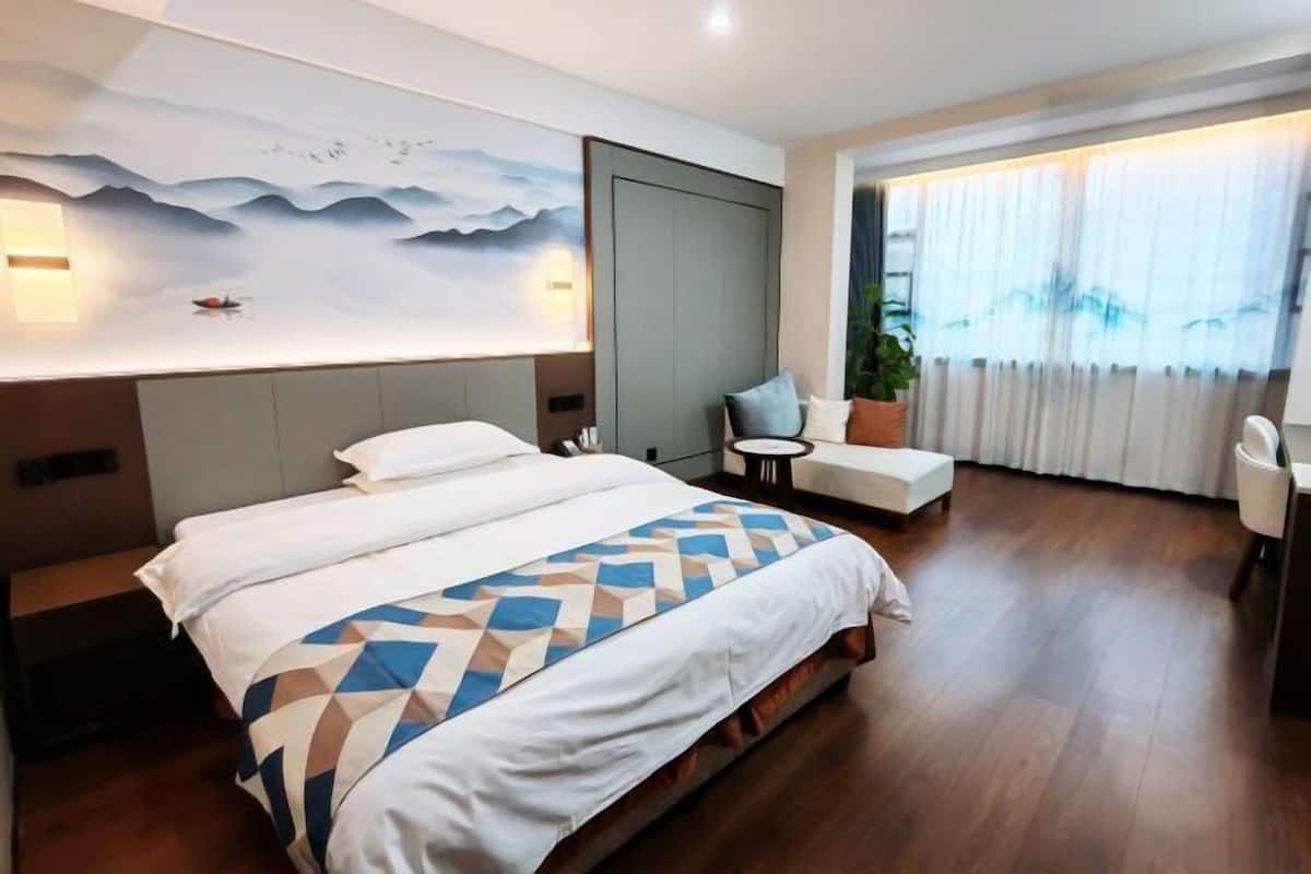 A hotel room with a large bed, a desk, a chair, and a view of the outdoors through a window.