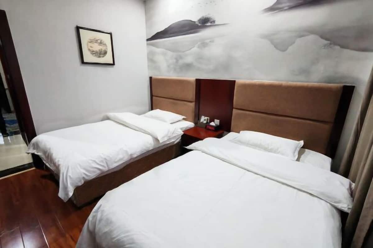 A hotel room with two single beds, a wooden floor, a nightstand, and a wall with a landscape painting.