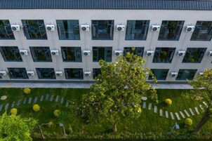 A modern building with multiple air conditioning units, a well-maintained lawn with trees, and a clear sky.