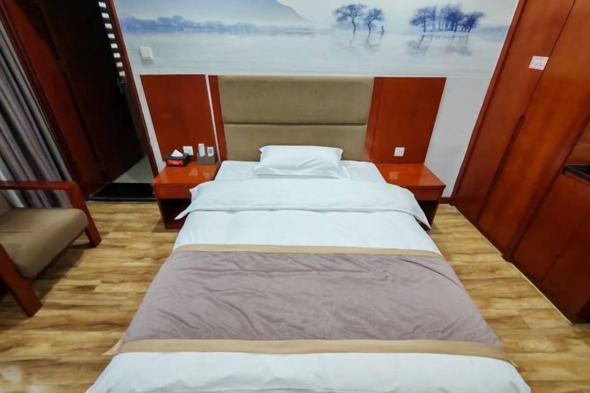 A hotel room with a bed, wooden headboard, nightstands, and a view of a snowy landscape through the window.