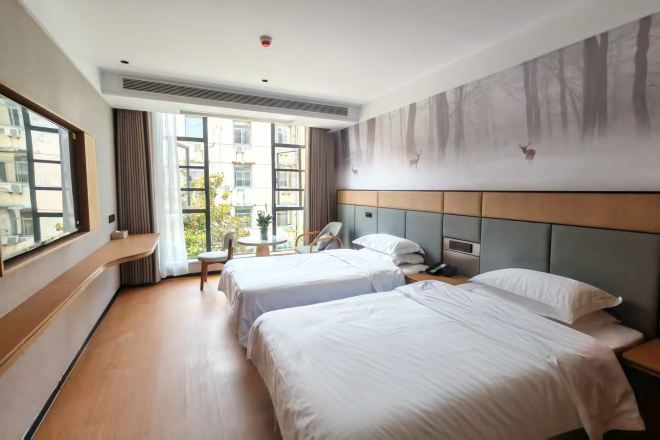 Habitación de hotel con dos camas, una ventana, vistas al exterior y un mural de un bosque en la pared.