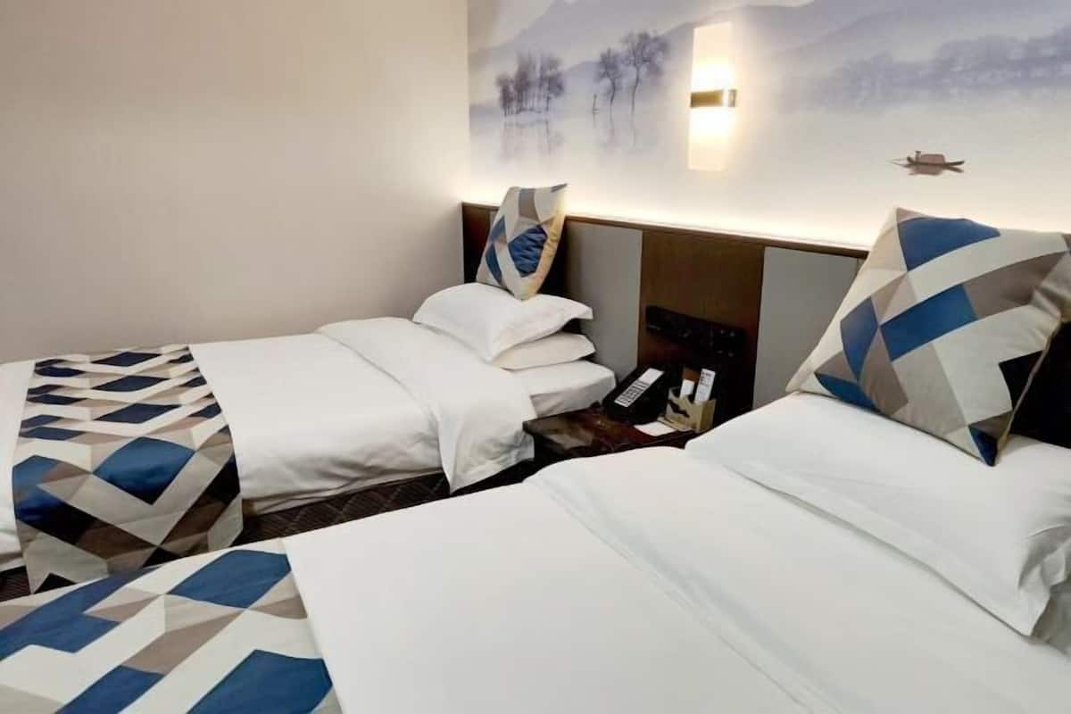 A hotel room with two beds, a nightstand, a wall-mounted phone, and a painting of a landscape.