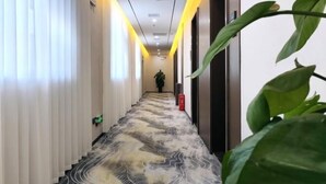 A hotel corridor with a patterned carpet, white walls, and a potted plant. - Taihe Jinghu Hotel (Taihe)