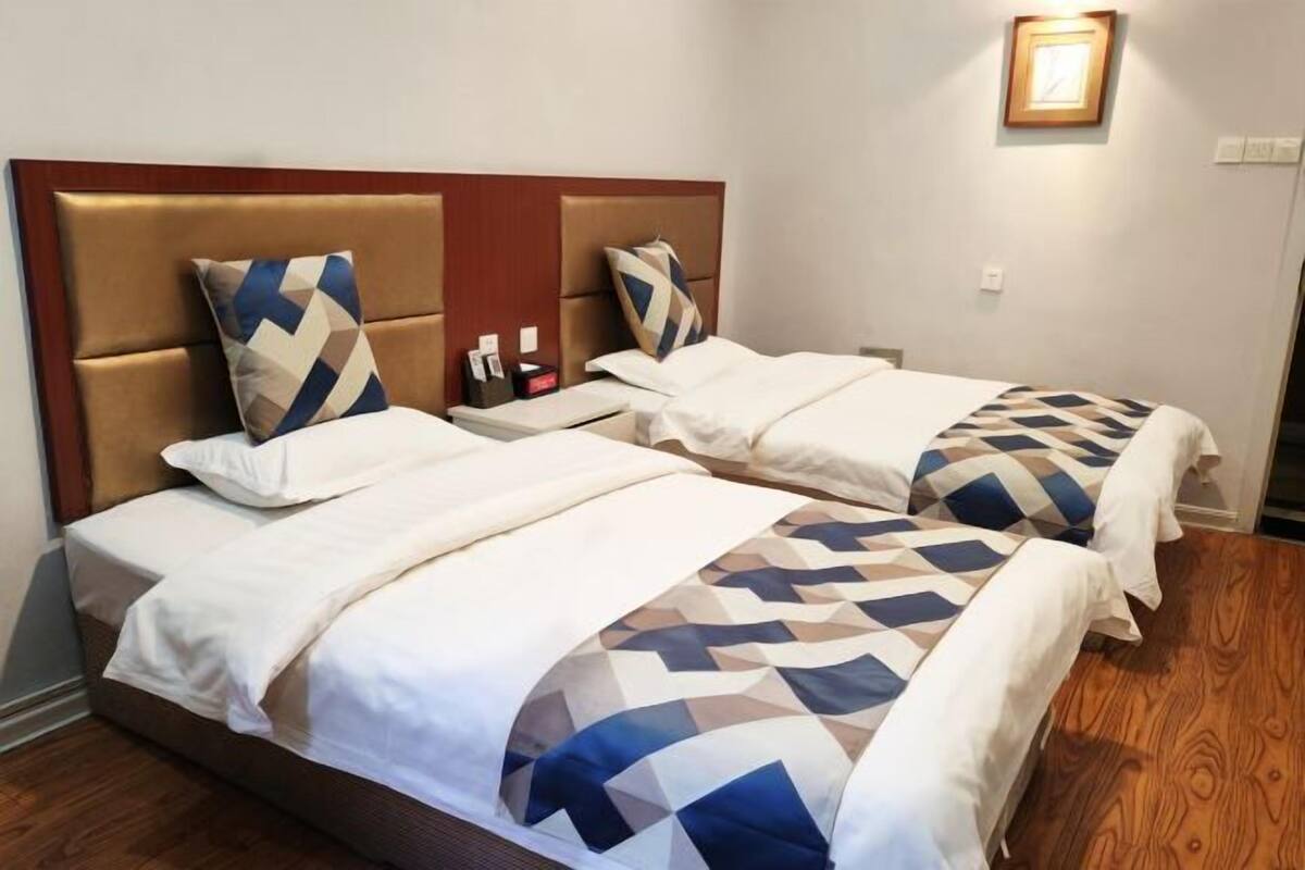 A hotel room with two beds, each with a headboard, a bedside table, and a lamp.