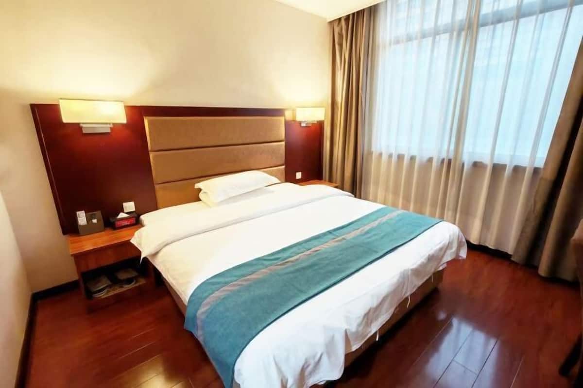 A hotel room with a bed, nightstands, a lamp, and a window with curtains.