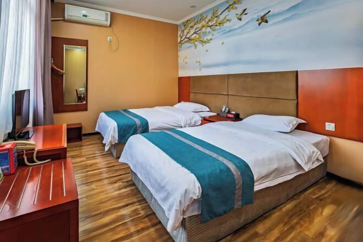 A hotel room with two beds, a wooden floor, a painting of birds on the wall, and a desk with a computer and a telephone.