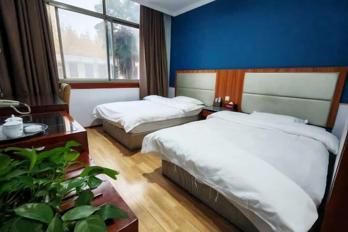 A hotel room with two beds, a desk with a telephone, and a window with curtains.