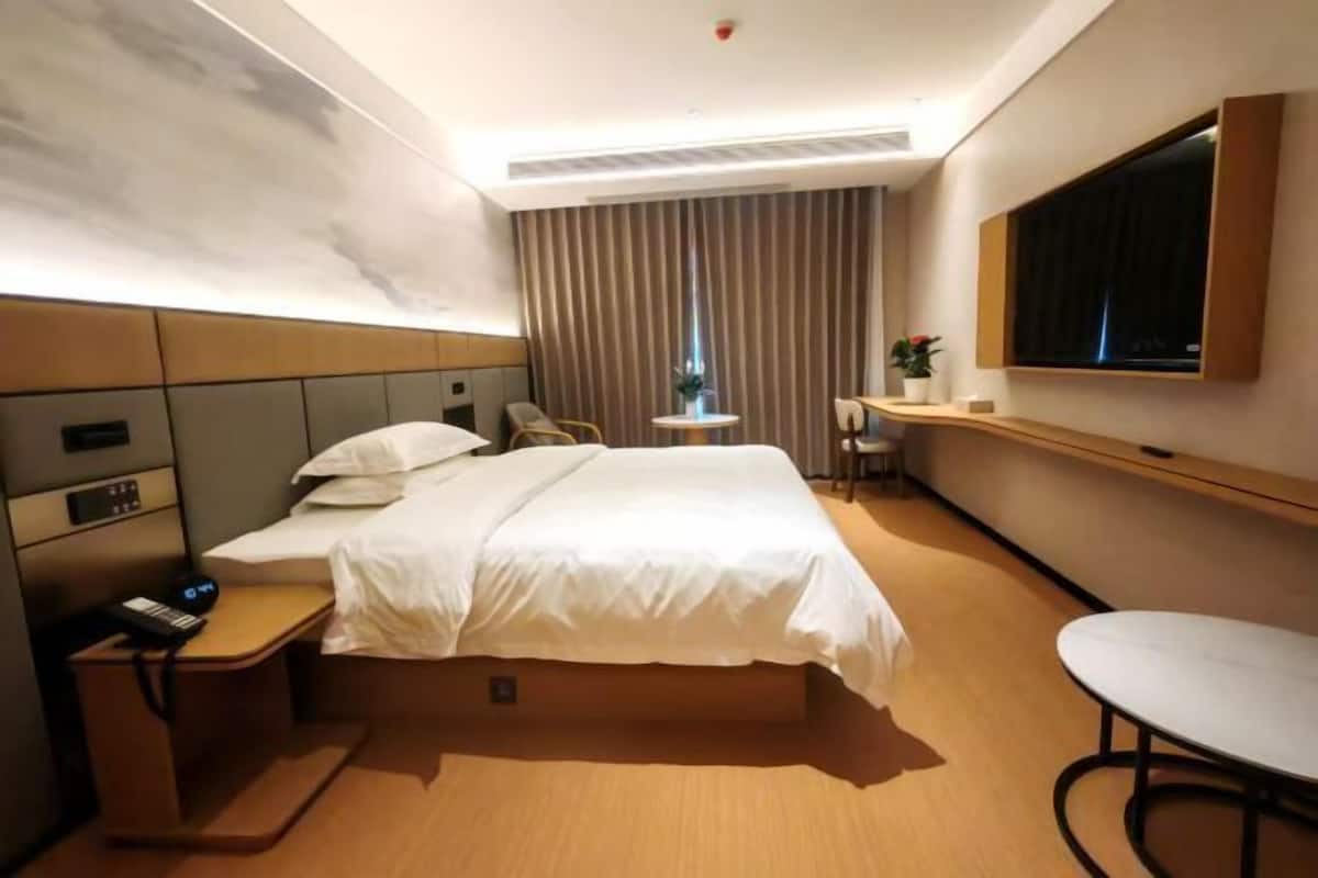 A hotel room with a bed, bedside table, TV, and a small table with chairs.