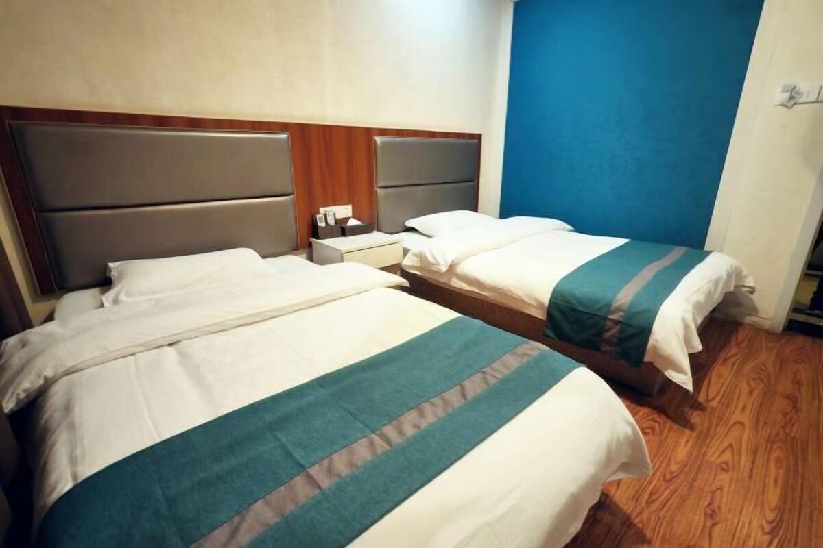 A hotel room with two beds, a wooden floor, and a blue accent wall.
