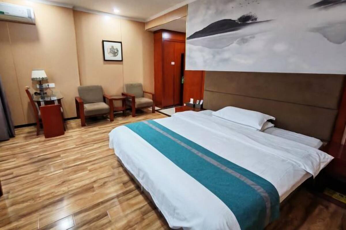A hotel room with a large bed, two chairs, a small table, and a painting on the wall.