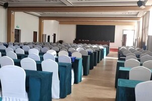 Un salón de conferencias con filas de mesas y sillas, una pizarra y una pantalla para proyector.