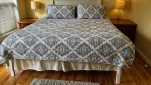 A bedroom with a patterned bedspread, two bedside lamps, and a wooden floor. - Charming  3B/R  Cottage on Malletts Bay (Colchester)