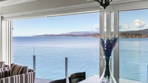 A room with a large window overlooking a body of water, a chandelier, and striped furniture. - Coastal View Sunset at SookePoint Cottages (Sooke)