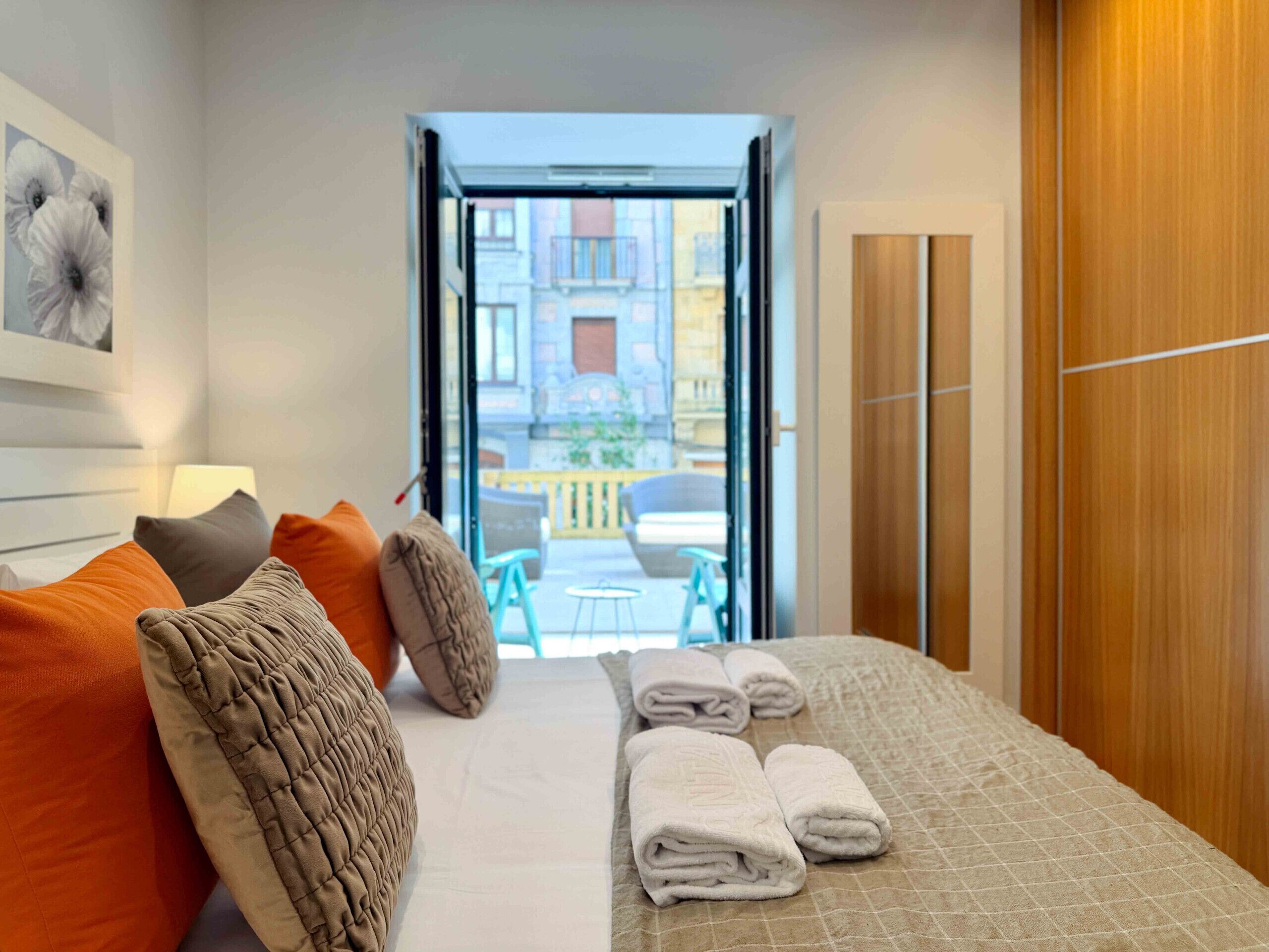 A hotel room with a bed, pillows, a view of the outside balcony, and a wooden wardrobe.