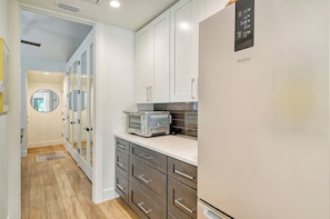 Una cocina moderna con refrigerador empotrado, microondas y tostadora. Se observan armarios blancos y piso de madera.