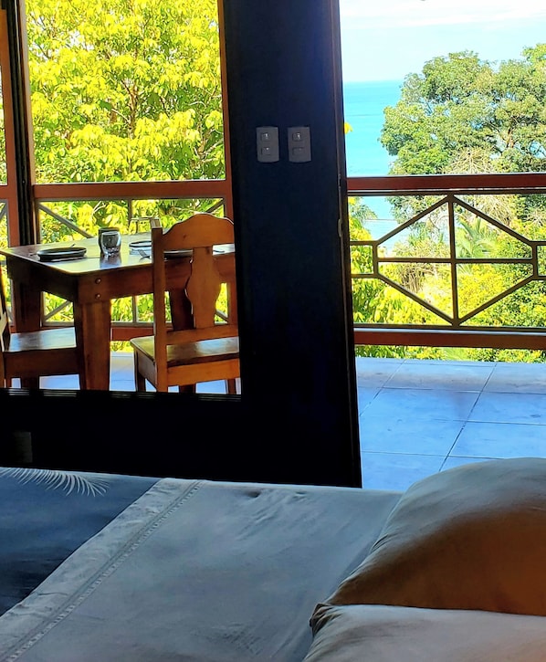 A room with a bed, a table with chairs, and a view of the ocean through a window.