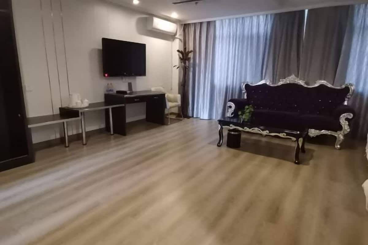 A modern living room with a dark sofa, a flat-screen TV, a desk, and a large window with curtains.