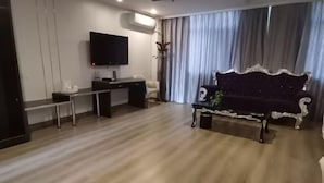 Ein modernes Wohnzimmer mit einem dunklen Sofa, einem Flachbildfernseher, einem Schreibtisch und einem großen Fenster mit Vorhängen.