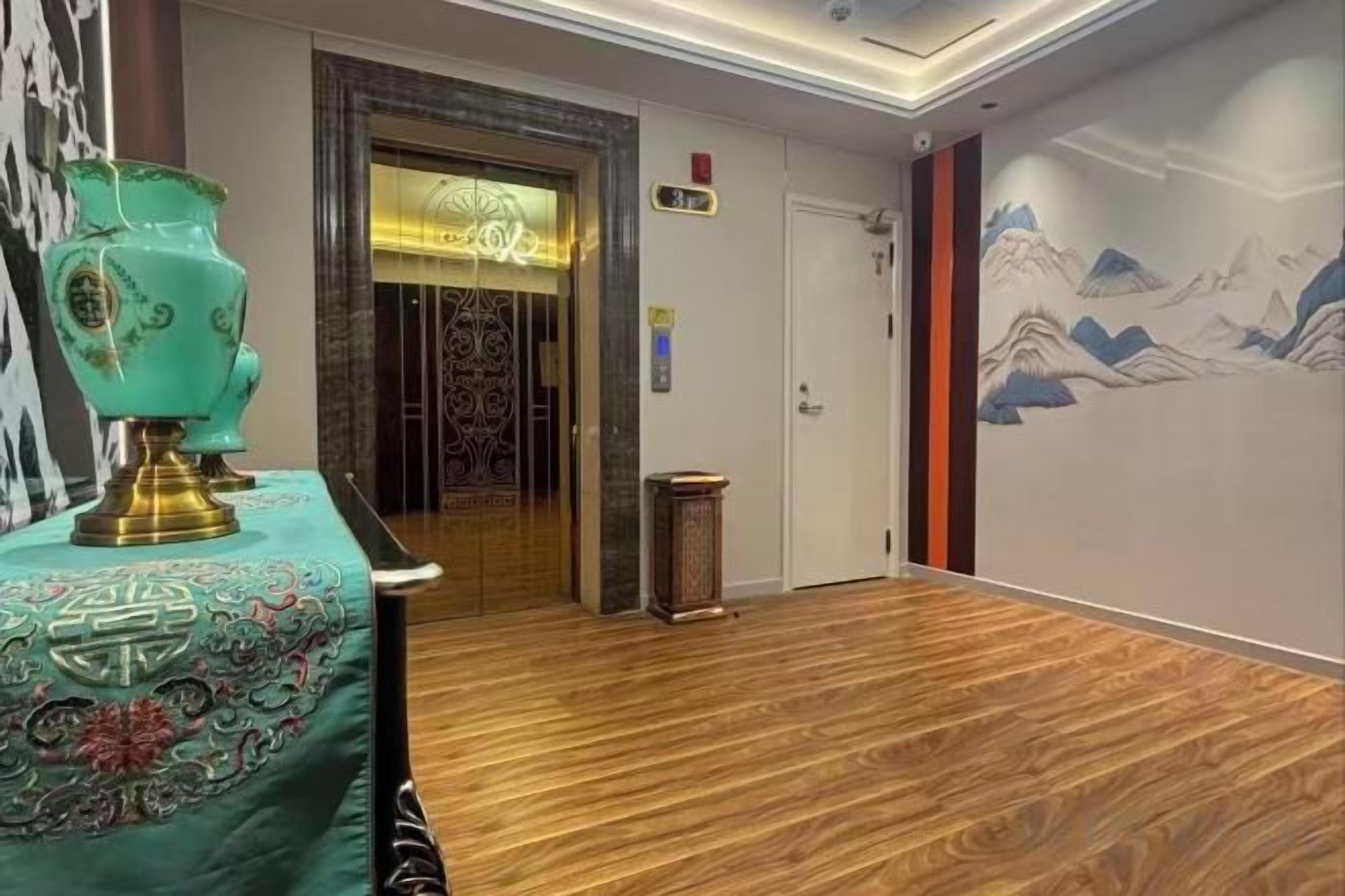 Un vestíbulo de hotel con piso de madera, una mesa decorativa con un jarrón, una puerta con un letrero y una pared con un mural de montañas.