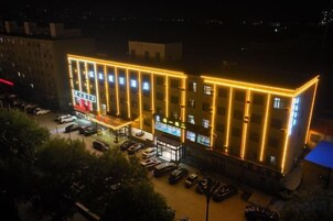 A multi-story building with a row of windows on the ground floor, a parking lot in front, and a small outdoor seating area.