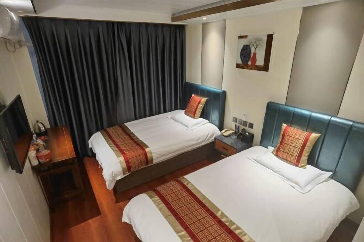 A hotel room with two beds, a desk, a chair, a TV, and a painting on the wall.