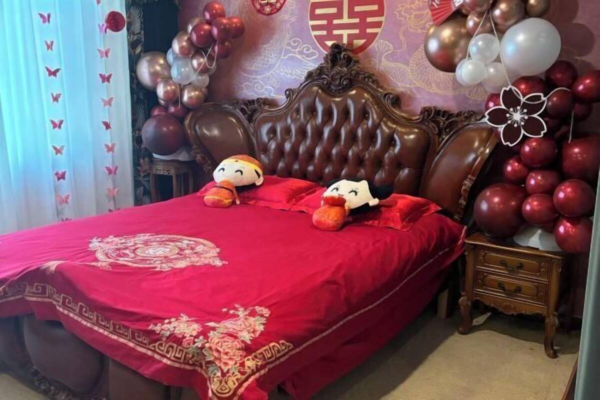 A bed with plush toys, a red bedspread, and a decorative wall with balloons.