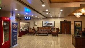 Eine Hotelhalle mit Marmorboden, einer roten Verkaufsmaschine, einer Sofagarnitur und gerahmten Kunstwerken an den Wänden.