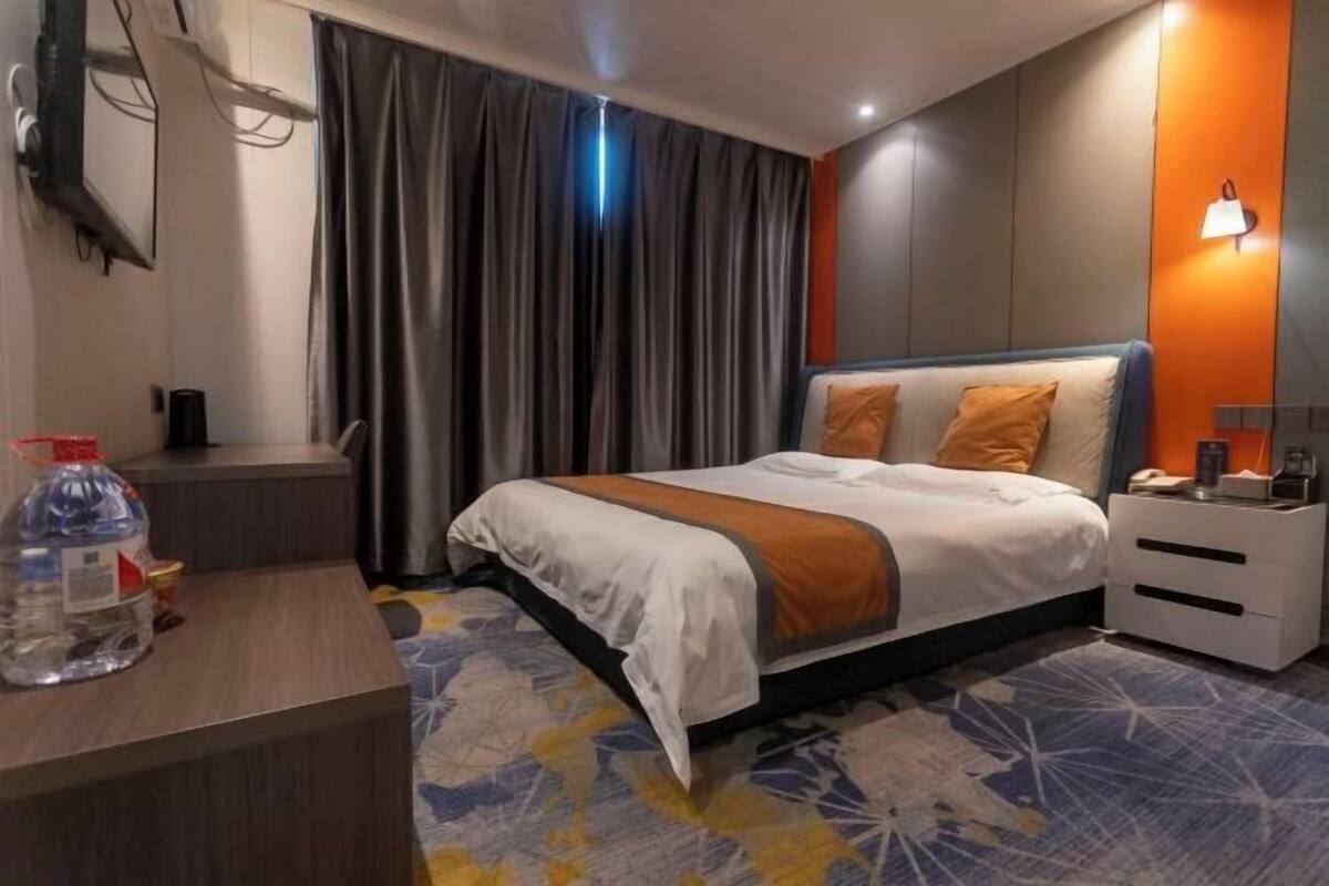 A hotel room with a bed, bedside table, and a desk with a bottle.