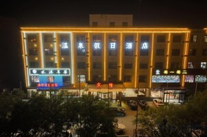 Un hotel de varios pisos con señalización iluminada, un estacionamiento y una pequeña zona de estar al aire libre.
