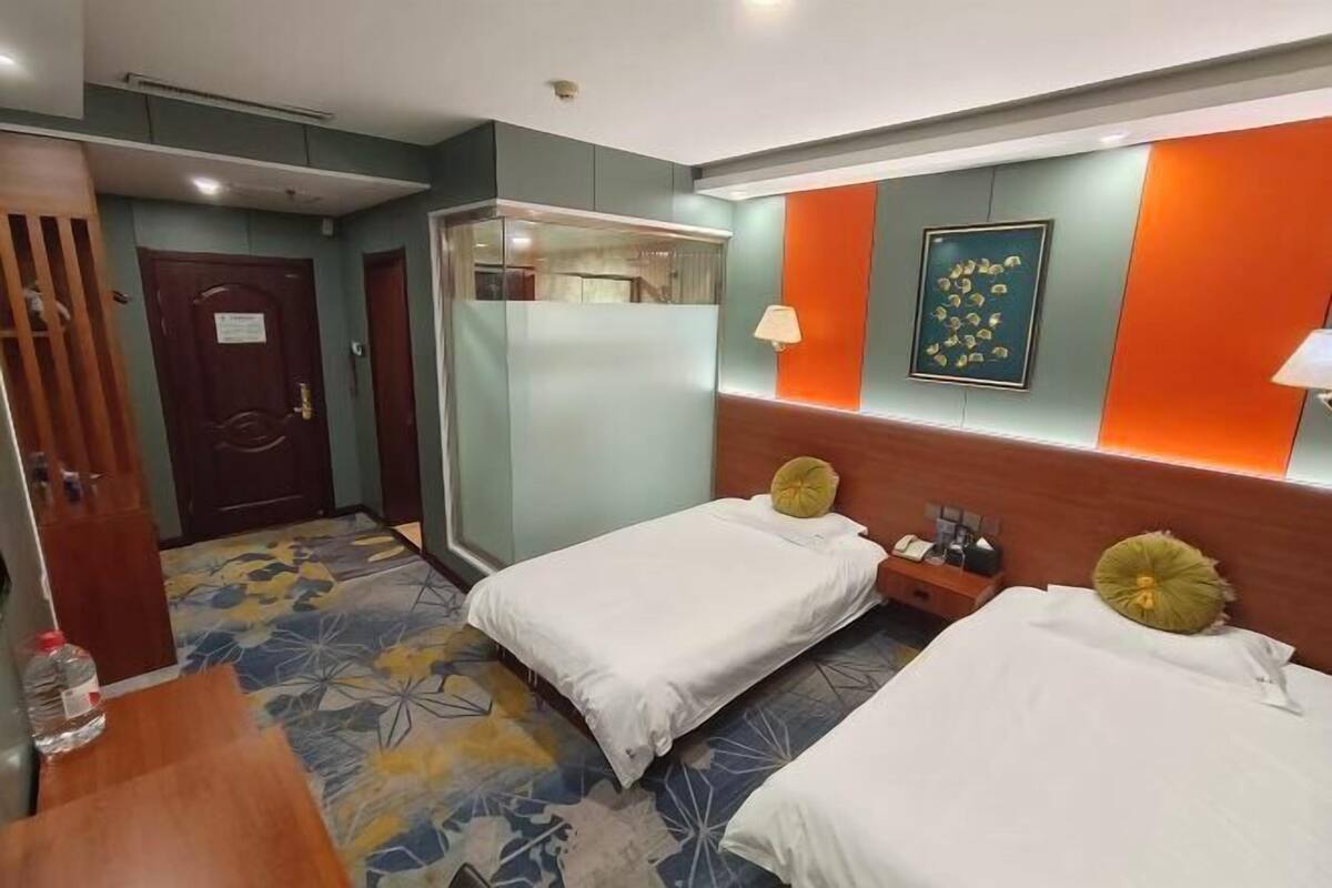 A hotel room with two single beds, a wooden desk, a mirror, and a bathroom door.