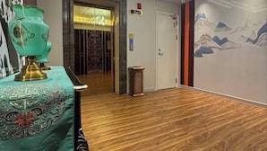 Eine Hotelhalle mit Holzboden, einem grünen Tisch mit einer Tischdecke und einer Tür mit einer Nummernschild, sowie einer Wand mit einem Berggemälde.