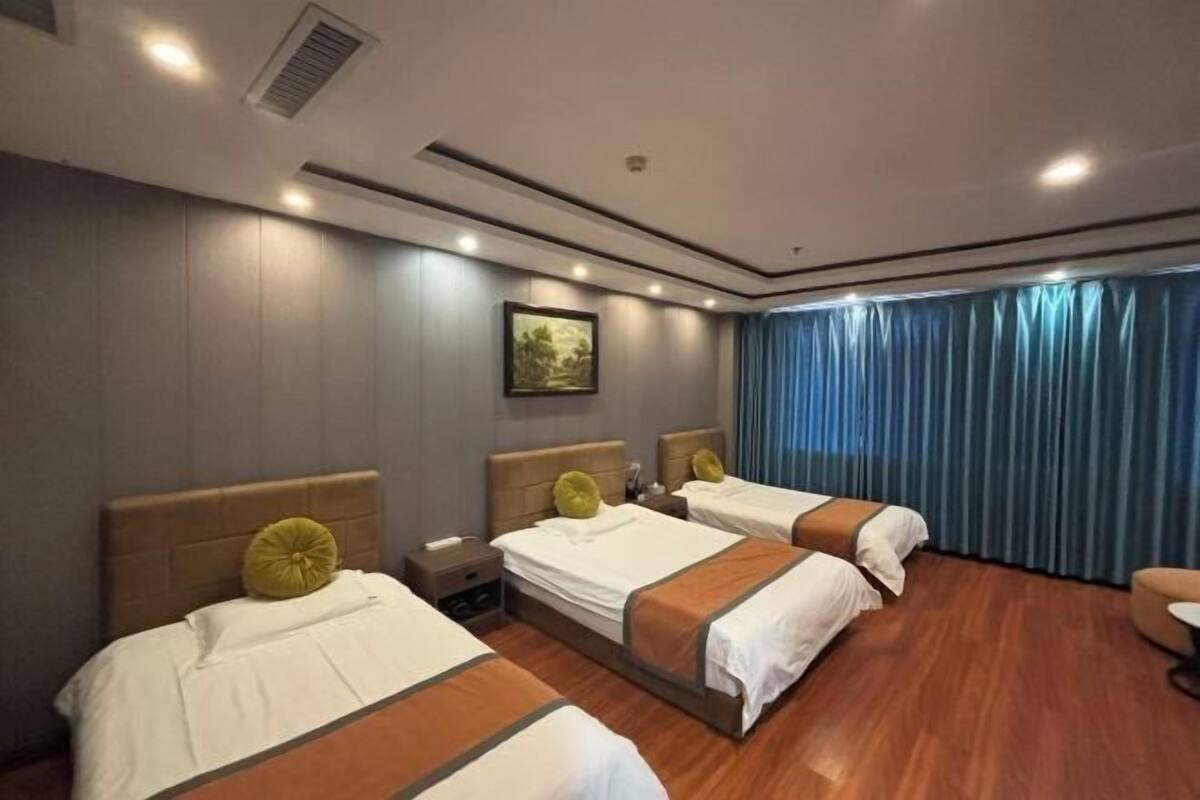 A hotel room with three beds, a painting on the wall, and a window with curtains.