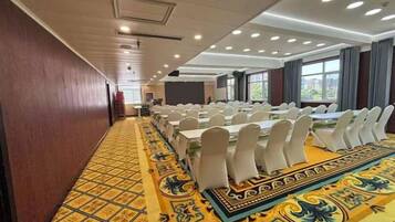 Un salón de conferencias con largas mesas, sillas blancas y una alfombra estampada.