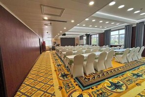 Un salón de conferencias con largas mesas, sillas blancas y una alfombra estampada.