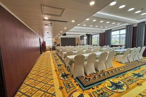 A conference room with long tables, white chairs, and a patterned carpet.
