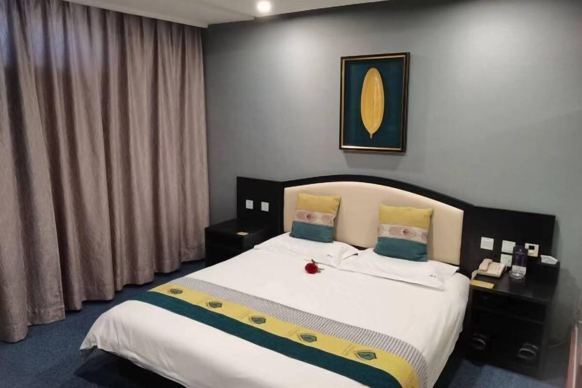 A hotel room with a bed, curtains, a nightstand, a phone, and a framed picture on the wall.