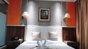 Ein Hotelzimmer mit einem großen Bett, zwei Nachttischlampen, einem gerahmten Bild an der Wand und einer dekorativen Schwanenfigur auf dem Bett.
