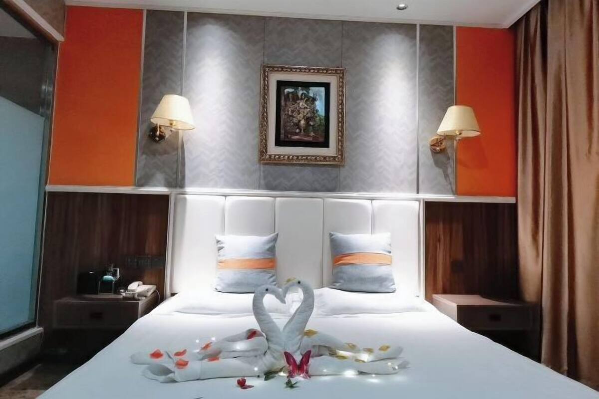 A hotel room with a large bed, two bedside lamps, a framed picture on the wall, and a decorative swan on the bed.