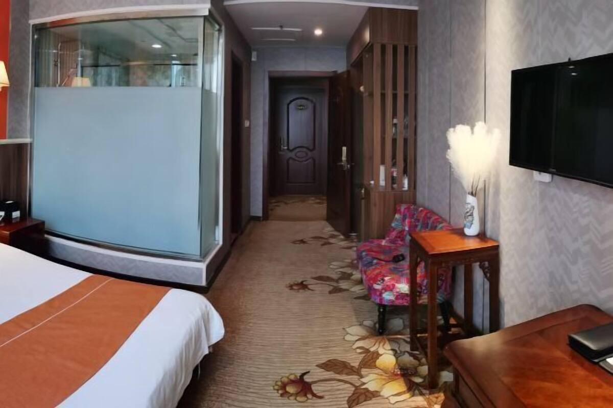 A hotel room with a large bed, a desk, a chair, a TV, and a decorative vase.