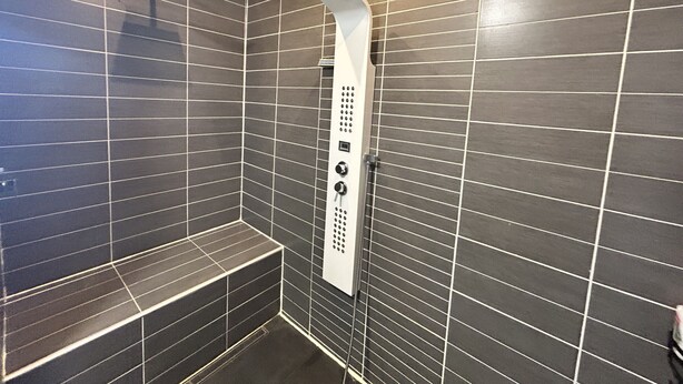 A modern shower area with a control panel, dark tiled walls, and a bench.