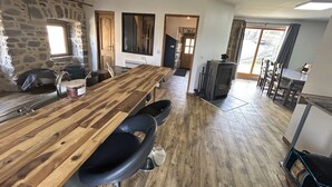 A spacious kitchen with a long wooden table, stone walls, and a large window.