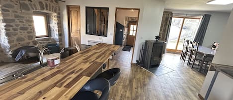 A spacious kitchen with a long wooden table, stone walls, and a large window.