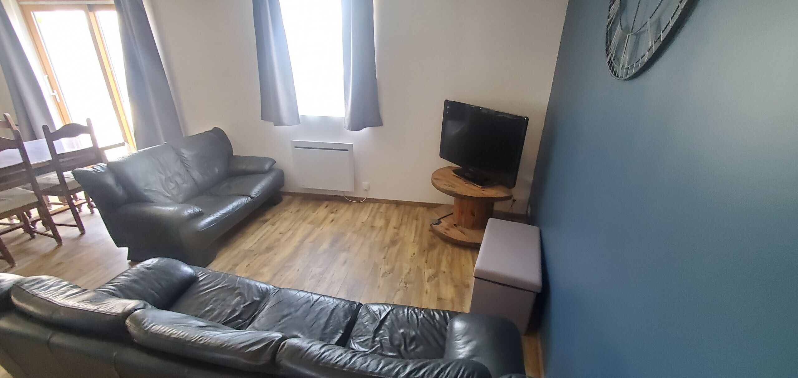 A living room with a leather sofa, a television on a wooden stand, and a dining area with a table and chairs.