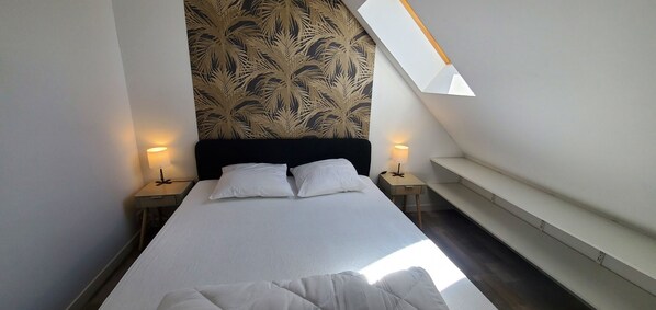 A bedroom with a bed, two bedside tables, a nightstand, a wall with a leaf pattern, and a skylight.