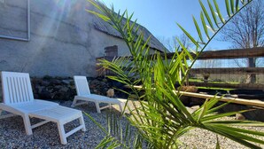 A patio area with two white lounge chairs, a stone wall, and a wooden fence.