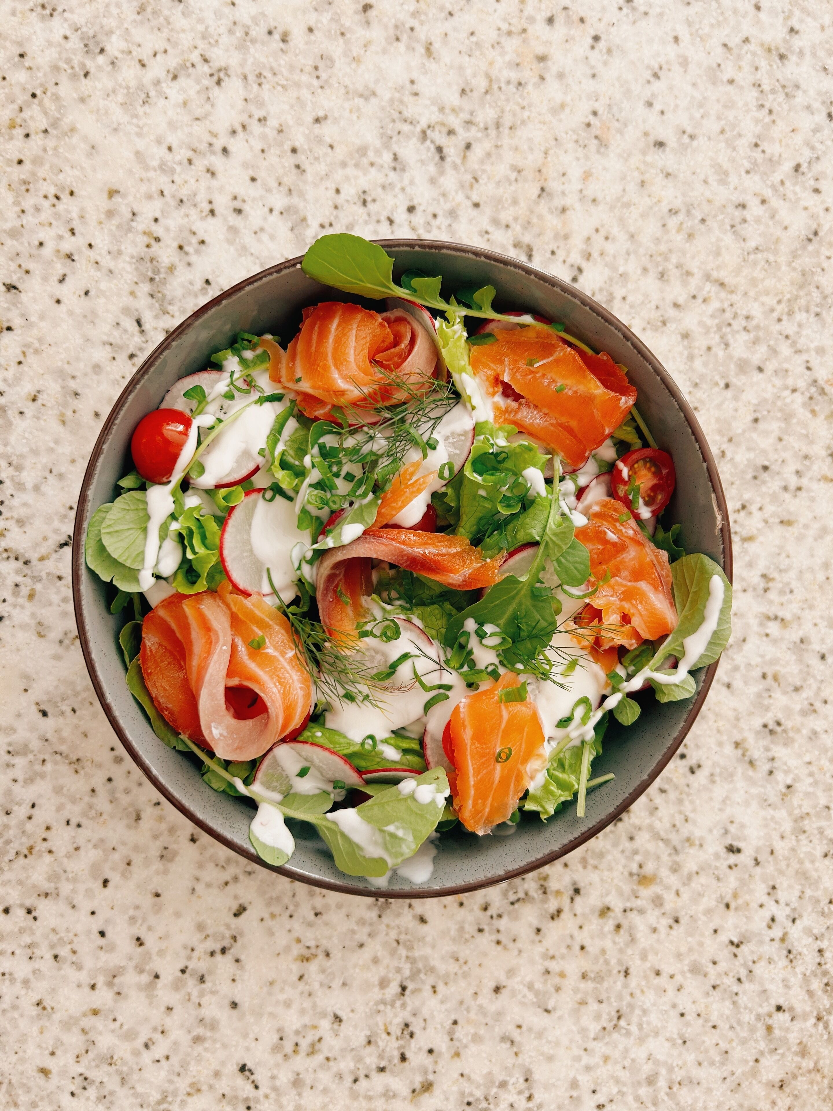 Een saladekom met zalm, radijsjes en groen.