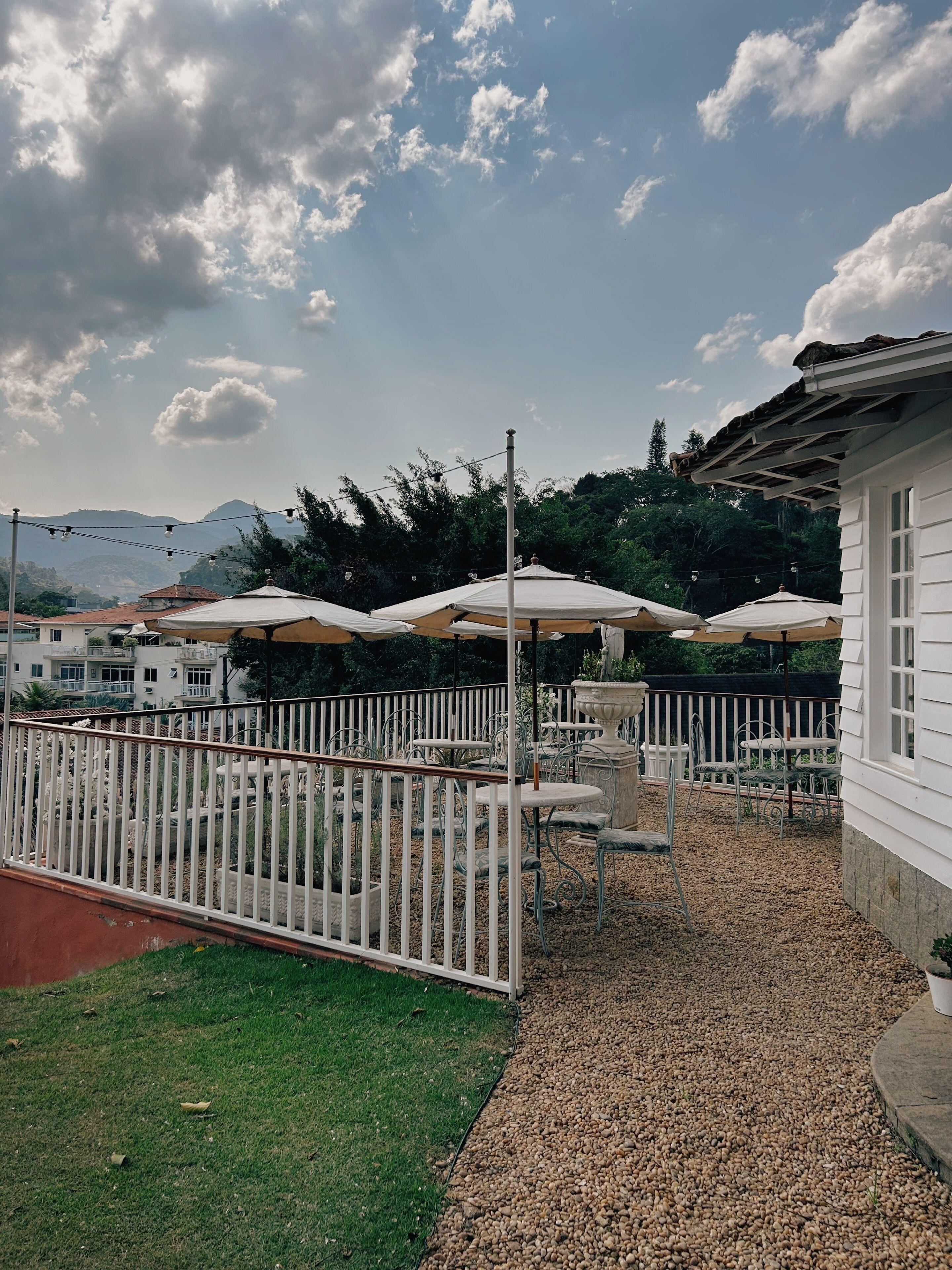 An outdoor patio area with tables and umbrellas, surrounded by a white fence, and a building with a white exterior.