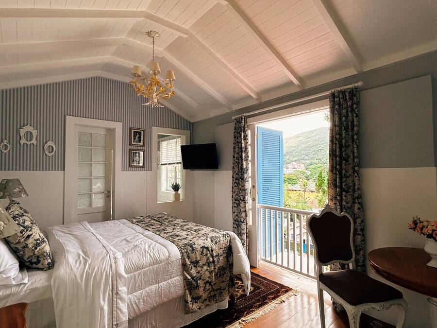 A bedroom with a bed, a chair, a table, and a balcony with a view.