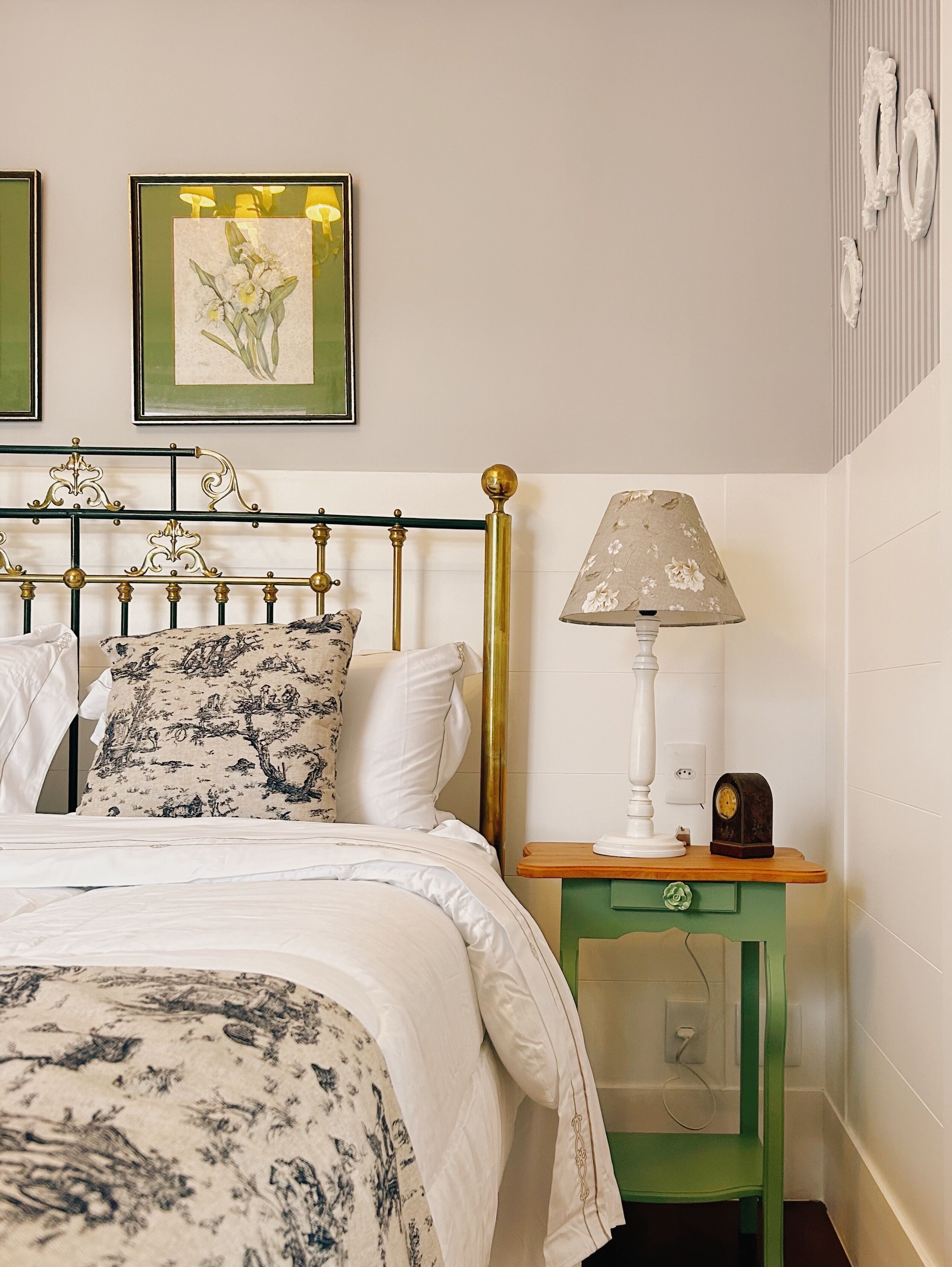 A neatly made bed with floral bedding, a green nightstand with a lamp, and a framed botanical print on the wall.