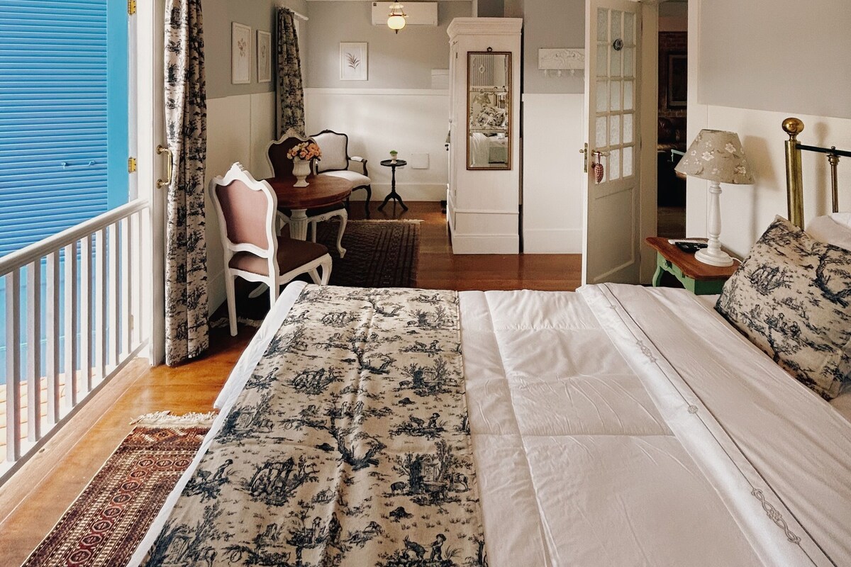 Un dormitorio con una cama grande, un candelabro, vistas a través de una ventana y un comedor con mesa y sillas.